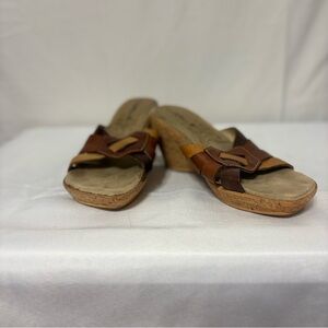 Brown leather wedge slide sandals with strappy uppers and cork-style soles.